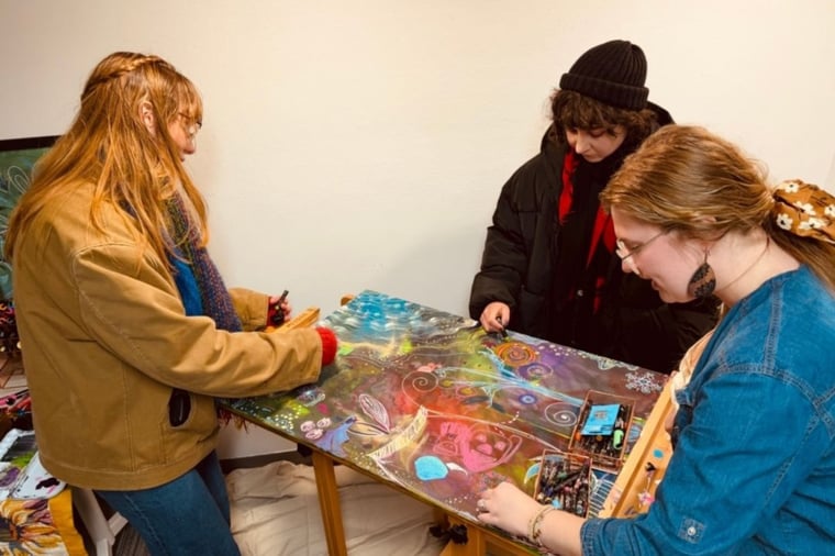 three people stand around a flat easel and doodle on a canvas