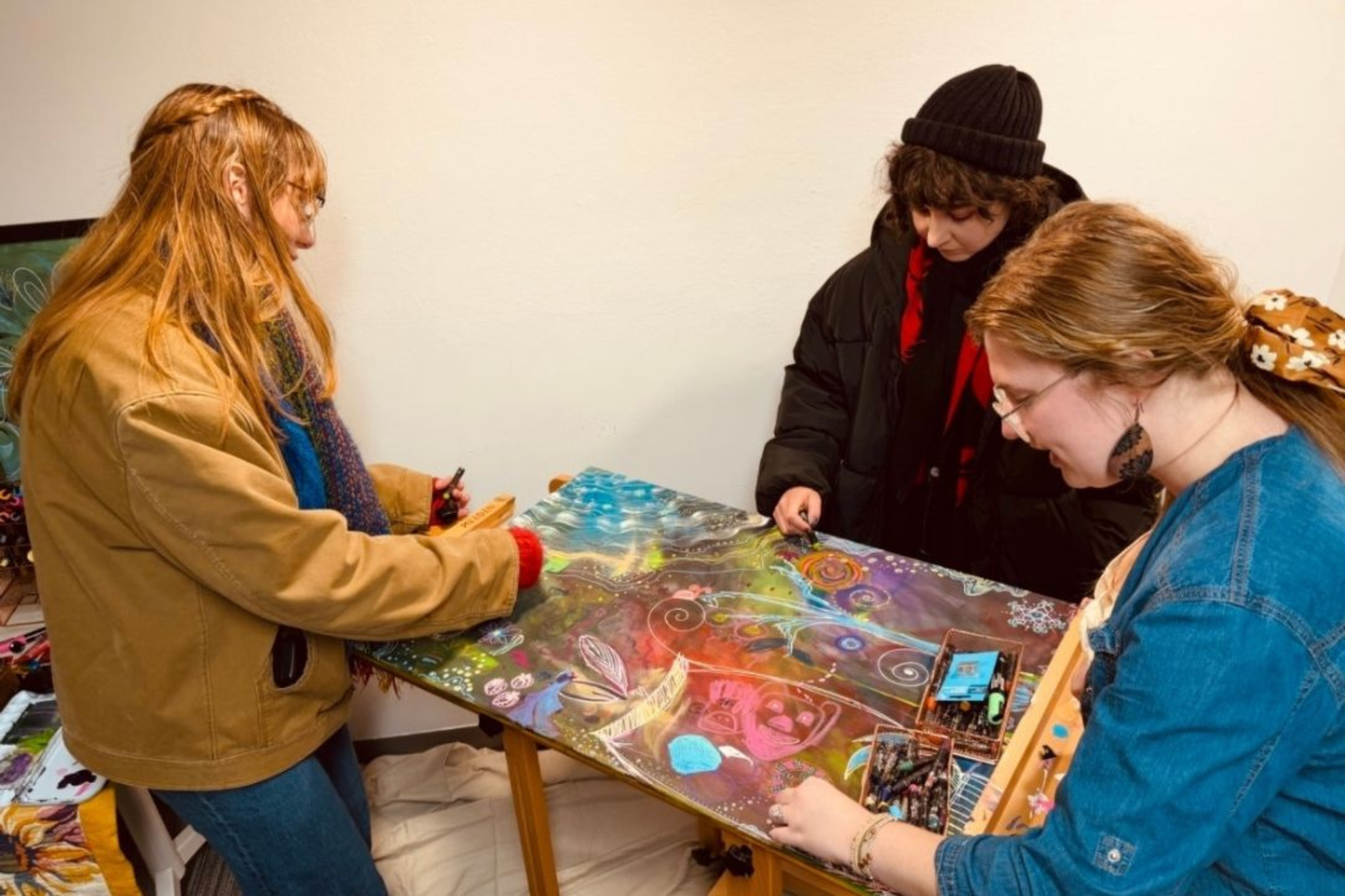 three people stand around a flat easel and doodle on a canvas